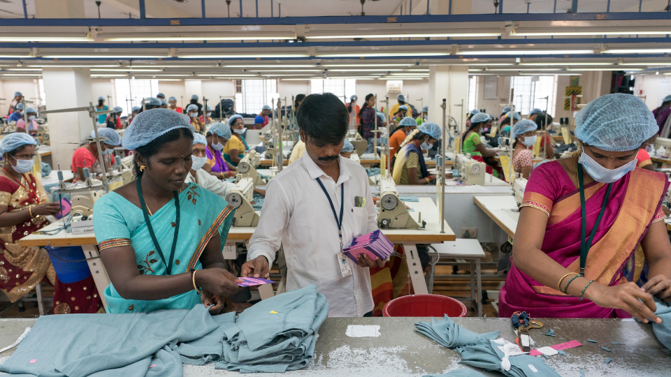 A man distributing an employee handbook to two workers measuring cloth at an apparel factory.
